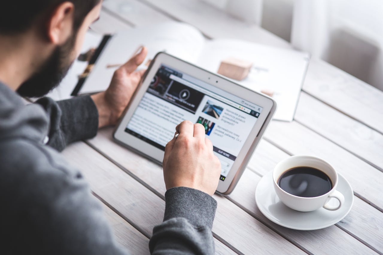heros-img A man uses a tablet to browse news while enjoying a cup of coffee, stylus in hand.